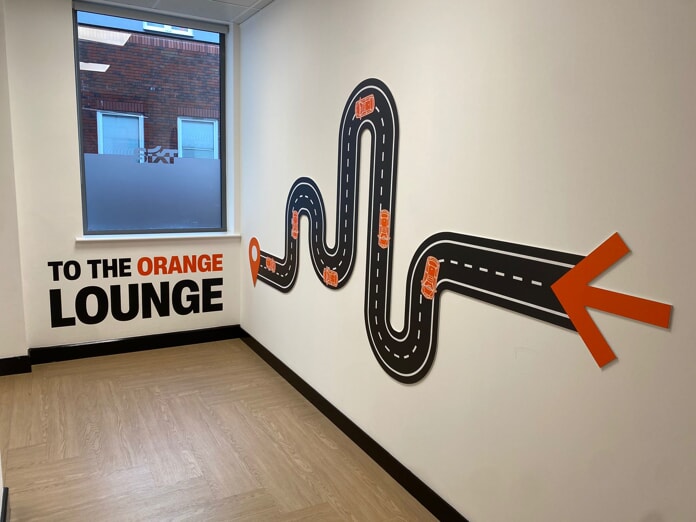 An image of a magnetic roadway wall graphic with little orange cars on it that reads "TO THE ORANGE LOUNGE"