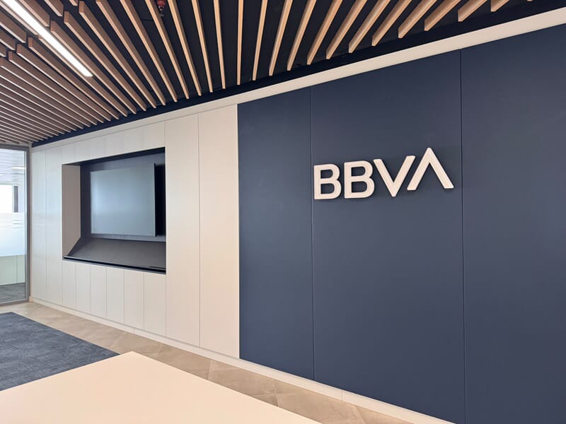 Shows the white BBVA interior wall mounted signage against a dark blue wall.